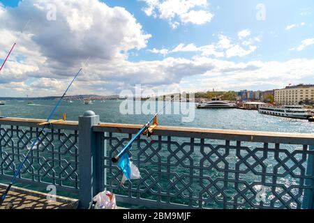 Fishing poles and line stick out over the Bosphorus River from the Galata Bridge as a cruise tour boats dock nearby in Istanbul, Turkey Stock Photo