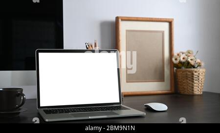 Photo of black working desk along with white blank screen computer laptop, books, notebook, pencil holder, picture frame, potted plant putting togethe Stock Photo