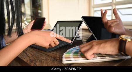 Cropped image of graphic designer team while selecting a color from color guide at the wooden meeting table over comfortable office as background. Stock Photo