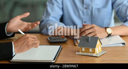 Cropped image of Real estate agent offer house insurance or house ownership to smart man in blue shirt  at the modern wooden table. Signing on agreeme Stock Photo