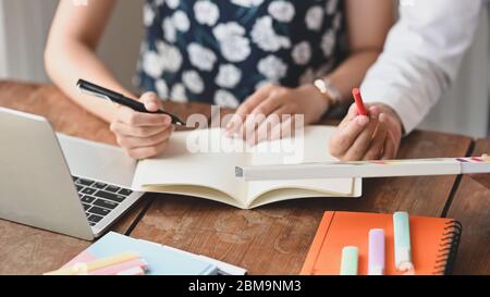 Cropped image of designer team discussing and writing on notebook while working/sitting together at the wooden working desk over comfortable living ro Stock Photo