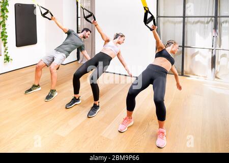 Three athletes doing Trx or suspended power pull exercises to stretch and strengthen their core muscles for increased flexibility in a health and fitn Stock Photo