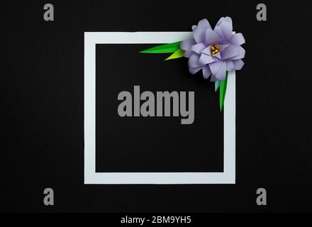 Square frame with lilac pastel color paper flower on black background. Flat lay, copy space, floral art Stock Photo