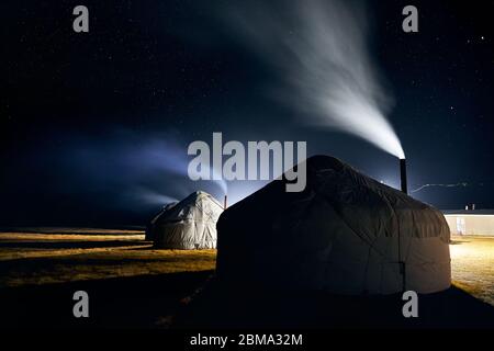 Yurt nomadic houses camp with smoke from the chimney at night sky with stars in Central Asia Stock Photo