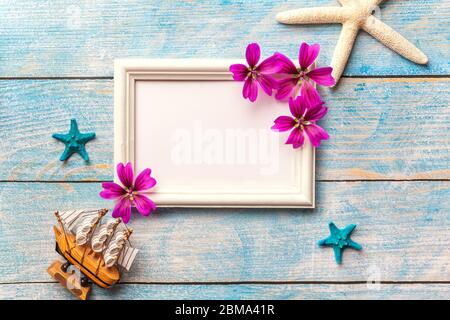 White wooden photo frame with purple flowers on blue old shabby background with copy space. Vacation greeting card with sea stars, seashell and ship. Stock Photo