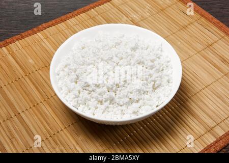 bowl with grainy cottage cheese on a straw tablecloth mat on the table Stock Photo