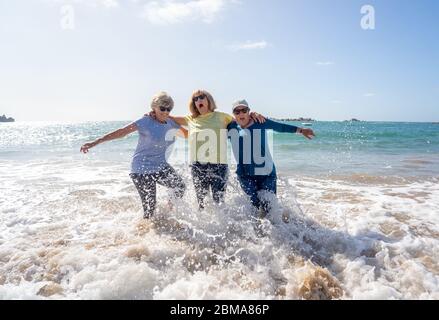 Group of senior retired women on their 60s and 70s falling in the water having fun on the beach. Older ladies laughing as they fall down loosing balan