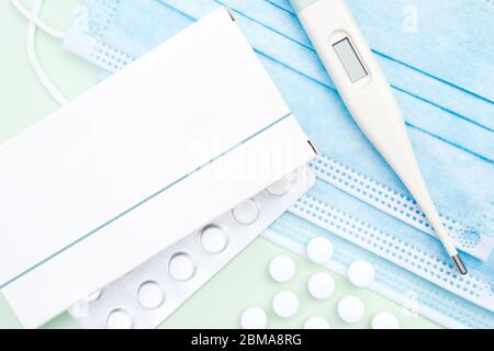 Medical items for coronavirus (covid-19) treatment and prevention laid out on green background. Thermometer, pills, blister, packaging and face mask Stock Photo