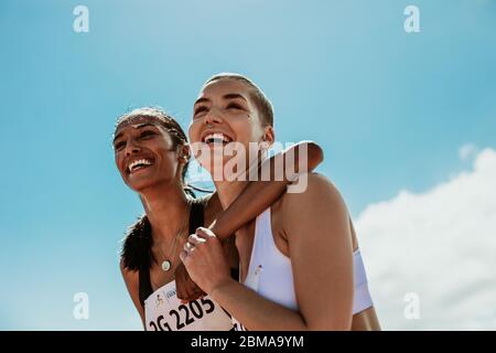 Two young woman athletes smiling outdoors. Female runners looking happy after winning the competition. Stock Photo