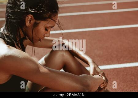 Female runner looking tired after workout session. Sportswoman feeling exhausted after a training session at running track. Stock Photo