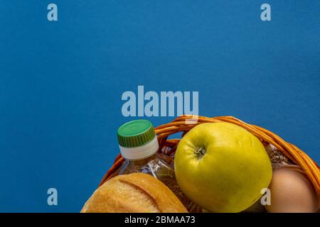 Donation, alms, healthy nutrition, humanitarian aid, pandemic, Covid-19 concept. Flatlay omposition of food in a wicker wooden basket on a blue Stock Photo