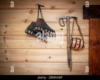 Vintage climbing leather boots and ice ax hang on a wooden wall. Antique Climbing Equipment Stock Photo