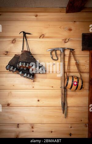 Vintage climbing leather boots and ice ax hang on a wooden wall. Antique Climbing Equipment Stock Photo