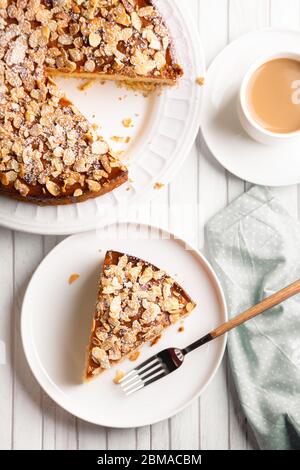 Almond and lemon cake with sliced almonds topping and a coffee cup on a white wooden table. Top view Stock Photo
