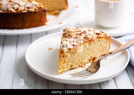 Almond and lemon cake with sliced almonds topping and a coffee cup on a white wooden table Stock Photo