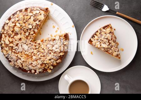 Almond and lemon cake with sliced almonds topping and a coffee cup on a concrete surface. Top view Stock Photo