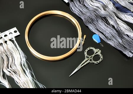 Accessories for needlework. Hoop, multi-colored threads, scissors, needle-threader on a black background. Copy space. Stock Photo