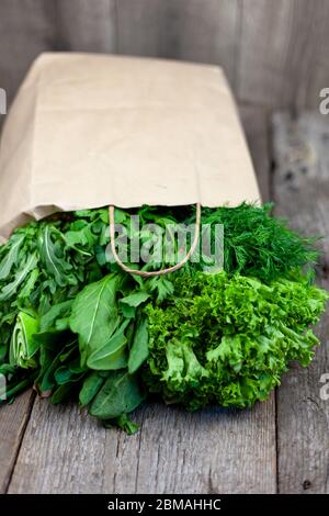 Fresh greens in a paper bag - green onions, dill, parsley, spinach, arugula, sorrel. Home delivery of food and fresh vegetables. Wooden background Stock Photo