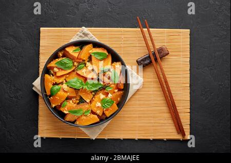 Pad Faktong or Thai Stir-fried Pumpkin in black bowl at dark slate background. Pad Phuk Tong is thailand cuisine dish with sliced Kabocha Squash, eggs Stock Photo