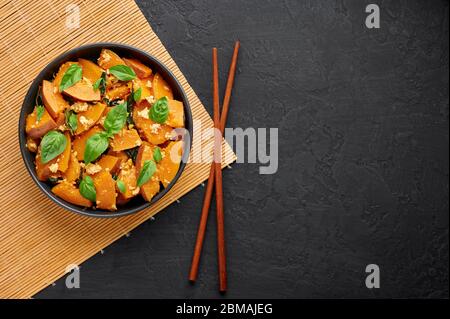 Pad Faktong or Thai Stir-fried Pumpkin in black bowl at dark slate backdrop. Pad Phuk Tong is thailand cuisine dish with sliced Kabocha Squash, eggs o Stock Photo