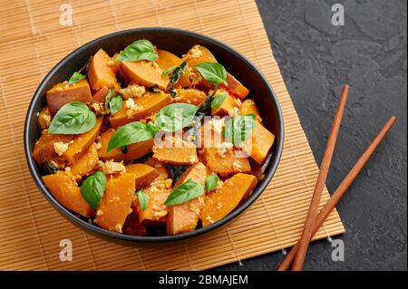 Pad Faktong or Thai Stir-fried Pumpkin in black bowl at dark slate background. Pad Phuk Tong is thailand cuisine dish with sliced Kabocha Squash, eggs Stock Photo