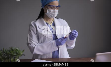 Doctor examines the blood tube of the diseased for coronavirus or covid 19 in the laboratory office. Female medical worker wearing medical protective Stock Photo