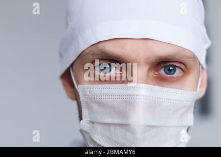 Tired young man doctor in mask during coronavirus. Dramatic portrait of medic, close-up