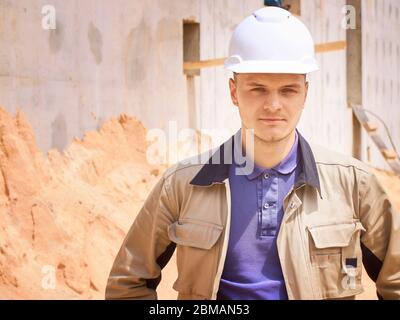 Caucasian civil engineer or construction worker in white hardhat stands opposite construction site Stock Photo