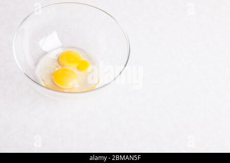 Two broken eggs in a glass transparent bowl on a white table close-up isolated for making an omelet or the main ingredient for baking desserts or doug Stock Photo