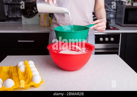 Making dough for Easter cake at home in the kitchen. Flour is poured out and sifted through a green sieve in female hands into a red bowl next to the Stock Photo