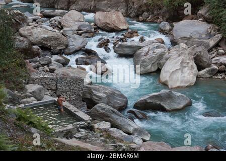Man having bath in natural hot springs pool and turquoise glacial rocky mountain river stream Stock Photo