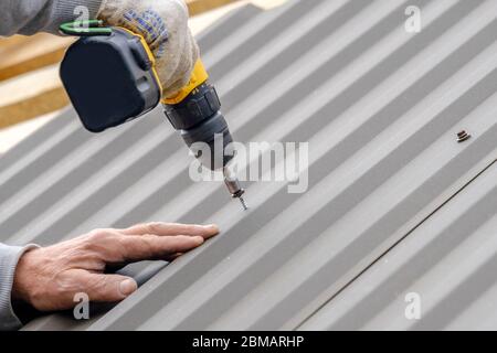 https://l450v.alamy.com/450v/2bmarhp/mens-hands-in-work-gloves-with-a-yellow-screwdriver-screw-the-roofing-sheet-to-the-roof-of-a-country-house-cordless-drill-2bmarhp.jpg