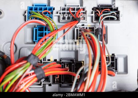 The metal case of the device with connectors and multi-colored electrical wires in the car during the repair of the system by an electrical engineer o Stock Photo