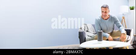 Senior Man Using Smart Home Speaker And Voice Assistant Stock Photo