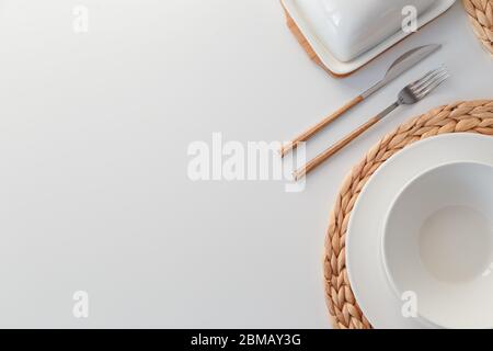 White ceramic tableware, fibre braided round placemat and cutlery set on white background. Scandinavian style. Stock Photo