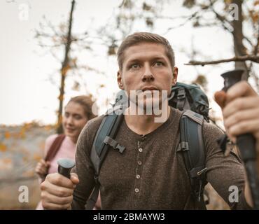 Man looking forward leaning on hiking pools. Family with backpacks walk together through the autumn forest Stock Photo
