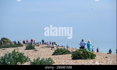 Littlehampton UK 8th May 2020 - People gather on the beach at Ferring near Worthing to watch the spitfire fly past in the distance to commemorate the VE Day anniversary during the lockdown restrictions of the coronavirus COVID-19 pandemic. It is 75 years since Victory in Europe over the Germans was announced during World War Two  : Credit Simon Dack / Alamy Live News Stock Photo