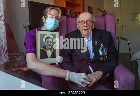 Care assistant Cat Buckley looks after 95 year old Second World War veteran Signalman Eric Bradshaw, who is in isolation after testing positive for covid 19, at Anchor's Millfield care home in Oldham, Greater Manchester, during a day of events to mark the 75th anniversary of VE Day. Stock Photo