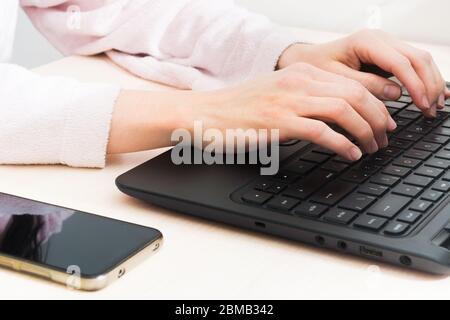 Woman in bathrobe sitting at the table at home with laptop and phone. Remotely work at home. Distance work. Online shopping Stock Photo