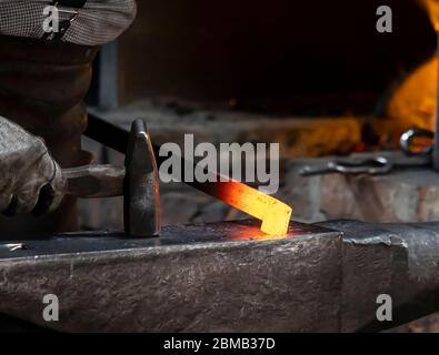 A blacksmith's hammer shaping red hot metal on an anvil. Stock Photo