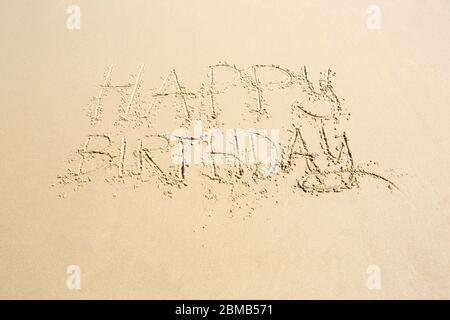 Happy birthday hand written on wet beach sand with copy space below in a conceptual image Stock Photo