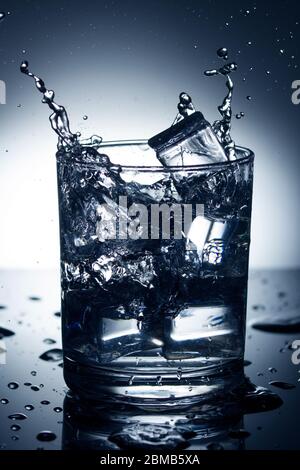 Glass of water with splash and ice on blue background. Stock Photo