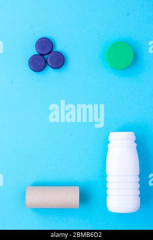 Recycling garbage. White plastic bottle, green cap, blue caps, finished paper roll arranged in a square shape on a blue background Stock Photo