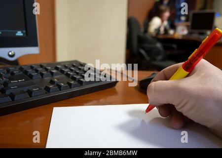 view of a writing pen in front of a white blank sheet of paper in the hand of an employee against the background of working people in the office Stock Photo