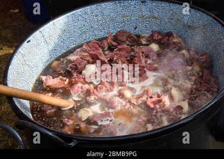 Very large cauldron cooking food during campfire, big pots on fire preparing during food festival. Tourist pot hanging over the fire on a tripod. Cook Stock Photo