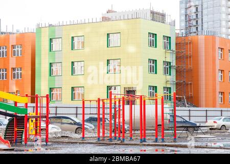 An empty children's playground with swings, a slide and horizontal bars of different colors in the courtyard of a kindergarten in a city landscape in Stock Photo