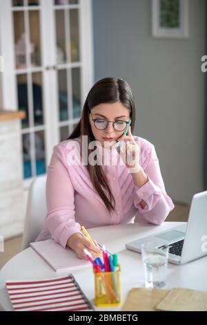 Woman in a pink blouse wearing eyeglasses sitting at the table Stock Photo