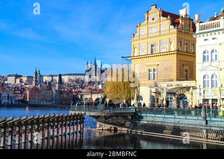 View over Vltava river towards Bedrich Smetana Museum and the historical center of Prague, with a crowd of tourists sightseeing at the riverbank. Stock Photo