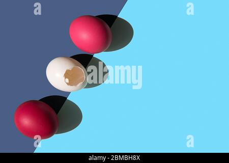 Three eggs are laid on the edge of the frame in a row. Two eggs are pink. One egg is white. the shell of a white egg has a hole in the middle. There i Stock Photo