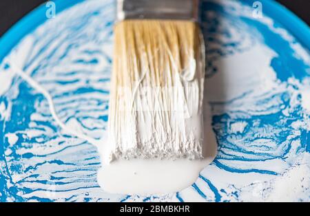 Close-up brush or paintbrush with white paint on surface of bristle and blue tin, can Stock Photo